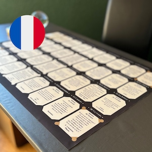 以下が含まれることがあります： フランス語のテキストが記載された白い八角形のカードのグリッドを備えた黒い長方形のゲームボード。各カードには、個人的な振り返りや人生のテーマに関連する番号付きの質問とプロンプトが含まれており、構造化されたレイアウトで配置されています。