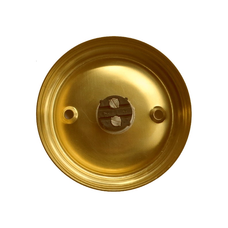 May include: A gold-colored doorbell button with two screw holes and a black plastic connector in the center.