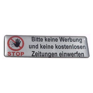 Könnte beinhalten: Ein silbernes Schild mit schwarzem Text, der "Bitte keine Werbung und keine kostenlosen Zeitungen einwerfen." lautet. Das Schild hat auch einen roten Kreis mit einem diagonalen Strich durch ihn und eine Hand mit ausgestrecktem Zeigefinger und Daumen. Der Text "STOP" befindet sich unter dem Kreis.