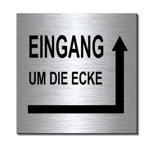 Könnte beinhalten: Ein silbernes Metallschild mit schwarzem Text, der "Eingang um die Ecke" lautet, was im Deutschen "Eingang um die Ecke" bedeutet. Ein Pfeil zeigt nach oben und rechts.
