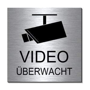Könnte beinhalten: Silbernes Metallschild mit einer schwarzen Silhouette einer Überwachungskamera und dem Text "VIDEO ÜBERWACHT".