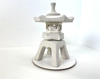 May include: White ceramic pagoda with a tiered design and a base with four legs. The pagoda is decorated with intricate carvings and a small finial on top.