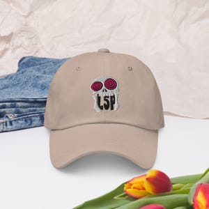 May include: A beige baseball cap with an embroidered skull design. The skull has red eyes and the text "LSP" is below the skull.