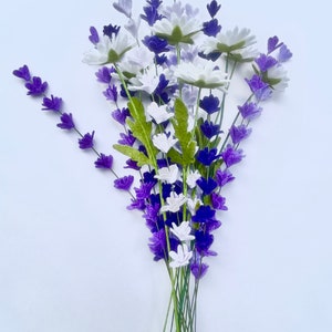 Op de afbeelding: Een boeket van paarse en witte viltbloemen. De bloemen zijn in een tros gerangschikt en hebben groene stelen.