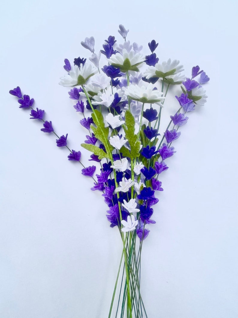 Op de afbeelding: Een boeket van paarse en witte viltbloemen. De bloemen zijn in een tros gerangschikt en hebben groene stelen.