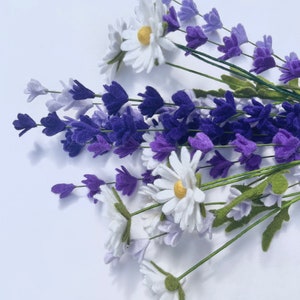 Op de afbeelding: Een boeket witte madeliefjes en paarse lavendelbloemen. De bloemen zijn gemaakt van vilt en hebben groene stelen.