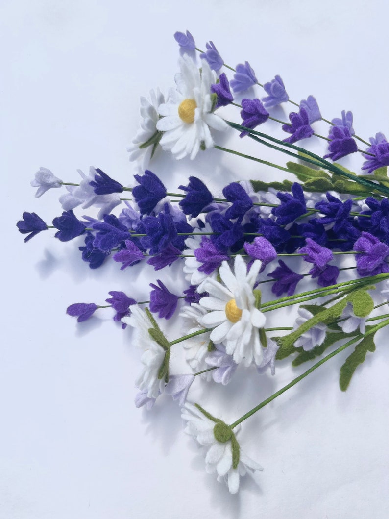 Op de afbeelding: Een boeket witte madeliefjes en paarse lavendelbloemen. De bloemen zijn gemaakt van vilt en hebben groene stelen.