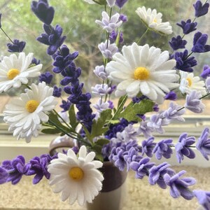 Op de afbeelding: Een boeket witte madeliefjes en paarse lavendelbloemen in een wit-paarse gestreepte keramische vaas.