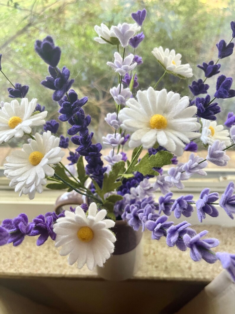 Op de afbeelding: Een boeket witte madeliefjes en paarse lavendelbloemen in een wit-paarse gestreepte keramische vaas.