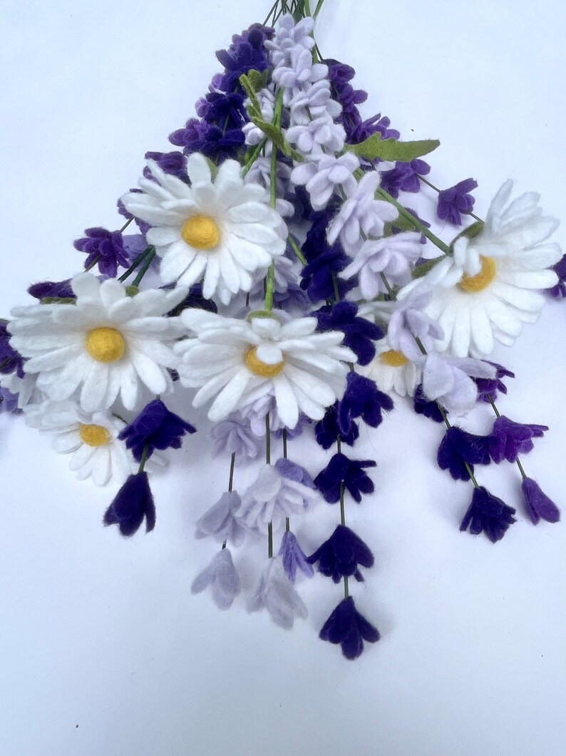 Op de afbeelding: Een boeket van viltbloemen met witte madeliefjes en paarse lavendel. De bloemen zijn in een tros gerangschikt en hebben een realistisch uiterlijk.