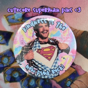 May include: A round pin with a Superman theme. The pin features a man revealing a Superman logo on his shirt, with the text "Kindness is the new Punk Rock!" and "cute coke superman pins <3". The pin has a pink and blue background.