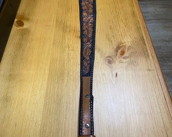 May include: A brown leather guitar strap with black stitching and a floral design. The strap is about 48 inches long.