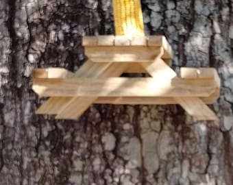 May include: A wooden bird feeder shaped like a picnic table with a single ear of corn on top.