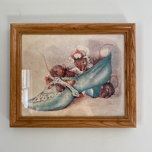 May include: A framed print of a vintage illustration featuring a blue shoe with a group of mice inside. The mice are peeking out of the shoe, and one is wearing a white bonnet.
