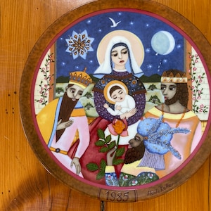 Peut inclure: Une assiette de Noël vintage avec une illustration bleue et blanche de la scène de la Nativité. L'assiette représente les trois mages, Marie, Joseph et l'enfant Jésus. L'assiette est décorée d'une bordure dorée et de l'année 1985. Le nom de l'artiste, "Heidi Keller", est imprimé au bas de l'assiette.