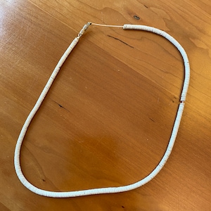 May include: A white beaded necklace with a gold clasp. The necklace is made of small, round beads that are strung together on a thin cord.