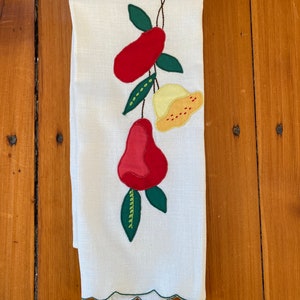 May include: White kitchen towel with a scalloped green edge, featuring an applique design of red and yellow fruit with green leaves. The fruit design is stitched onto the towel with black thread. The towel is made of a linen-like material.
