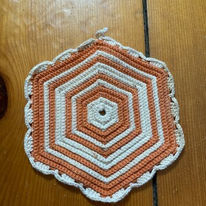May include: A crocheted doily in orange and white with a scalloped edge.