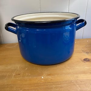 May include: A blue enamel pot with a white interior and black rim. The pot has two handles on the sides.