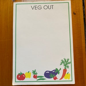 May include: A white notepad with a green border and the text "VEG OUT" in black. The bottom border features a colorful illustration of vegetables, including a red tomato, a yellow bell pepper, a green radish, a purple eggplant, and an orange carrot.
