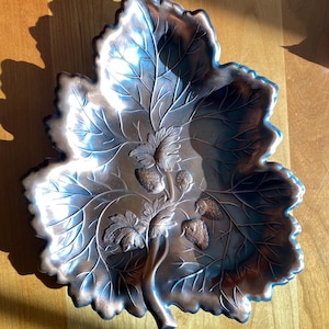 May include: A copper leaf-shaped dish with a raised design of a vine with strawberries. The dish is a decorative piece with a rustic, vintage look.