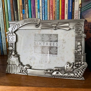 May include: A silver-toned picture frame with an ornate design featuring a clock, a dog, and a bed. The frame is labeled "My Family" and "SIXTREES London New York 3 1/2" x 5" ".