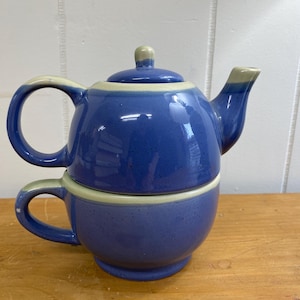 May include: A blue and white ceramic teapot and cup set. The teapot has a lid and a spout. The cup has a handle. The set is on a wooden surface.