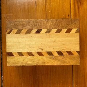 Op de afbeelding: Een houten doos met een decoratieve inleg van verschillende houtsoorten. De inleg is in een chevron-patroon.