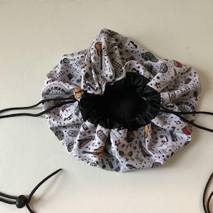 May include: A round, white drawstring bag with a black interior. The bag is patterned with musical instruments and notes in various colours. Black drawstrings are visible, and the bag is open.