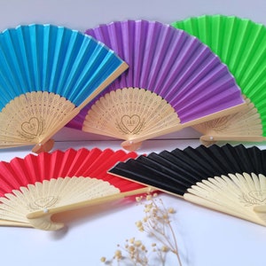 May include: Five hand fans with wooden handles and decorative designs. The fans are in various colors, including blue, purple, green, red, and black.
