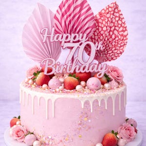 May include: A pink birthday cake with white icing drips, decorated with fresh strawberries, pink roses, and a "Happy 70th Birthday" topper. The cake is adorned with sprinkles and edible pearls. A celebratory dessert.