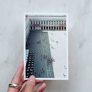 Op de afbeelding: Een luchtfoto van een groot, open plein met een gebouw op de achtergrond. Het plein is in twee delen verdeeld door een diagonale lijn. Het deel links is schaduwrijk, terwijl het deel rechts zonnig is. Er lopen mensen over het plein.