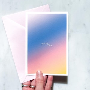 Könnte beinhalten: Eine Grußkarte mit einem Farbverlauf in Blau, Rosa und Gelb, mit dem Schriftzug "next chapter" in einer zarten Schriftart. Dazu gehört ein passender rosa Umschlag, ideal zum Versenden einer nachdenklichen Nachricht.
