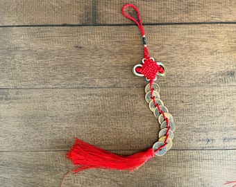 May include: A red Chinese knot ornament with a tassel and a string of coins. The ornament features a decorative knot with gold accents and a long red tassel. The coins are round with square holes.