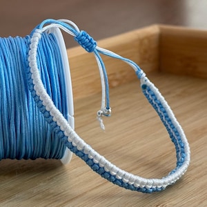 May include: A blue and white braided friendship bracelet with a silver bead accent.