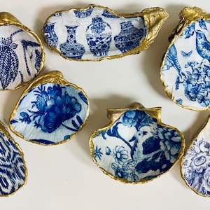 Può includere: Sette conchiglie di ostriche decorative con bordi dorati e disegni a motivi blu e bianchi. I motivi includono disegni floreali, uccelli e motivi geometrici.
