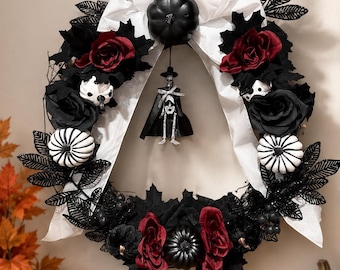 May include: A decorative wreath featuring a central hanging skeleton figure, a black pumpkin, and white ribbon. The arrangement includes black and deep red artificial roses, black glittered leaves, and small black and white striped pumpkins.