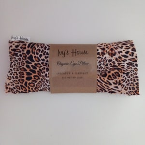 May include: An eye pillow with a leopard print pattern in brown and black. The pillow is wrapped with a brown paper label that reads "Ivy's House Organic Eye Pillow Lavender & Flaxseed Use Hot or Cold."