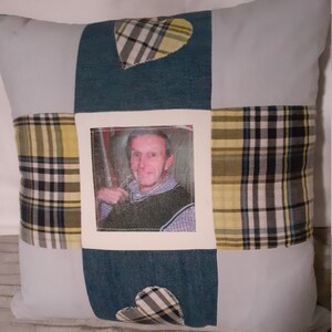 May include: A white cushion with a patchwork design featuring a photo of a man in the centre. The patchwork includes blue denim fabric, yellow and black checked fabric, and white fabric with a heart shape cut out. The heart shapes are filled with the same yellow and black checked fabric.