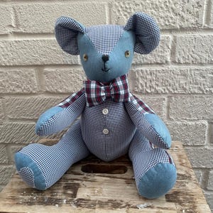 May include: A handcrafted teddy bear with a blue denim face and ears, and a gingham body. The bear has a red and white plaid bow tie and button details. A charming, handmade plush toy.
