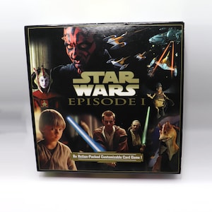May include: A square Star Wars Episode I customizable card game box featuring a collage of characters including Darth Maul, Queen Amidala, young Anakin Skywalker, Obi-Wan Kenobi, Qui-Gon Jinn, and Jar Jar Binks, with starships and lightsabers.
