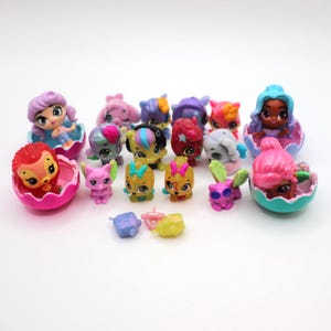 May include: A collection of colorful miniature figurines, including dolls and animal-like characters, some emerging from egg-shaped containers. The figurines feature various colors like pink, blue, yellow, and purple, with detailed facial features and accessories.