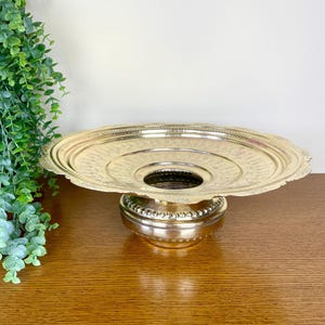 May include: A gold metal decorative stand with a round top and a circular base. The stand has an intricate design and is perfect for displaying flowers or other decorative items.