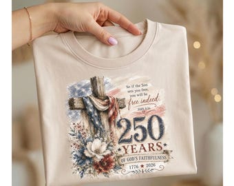 Peut inclure: Un t-shirt beige avec un motif graphique. Le motif comprend une croix en bois drapée d'un drapeau américain et le texte "So if the Son sets you free, you will be free indeed," "250 YEARS OF GOD'S FAITHFULNESS 1776 2026."