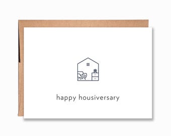 May include: A white greeting card with a brown envelope featuring a black line art icon of a house interior containing a chair, a cabinet, and a plant. Below the icon, the text reads "happy housiversary" in a simple, lowercase sans-serif font.