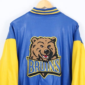 May include: A blue and yellow varsity jacket featuring a large embroidered patch on the back. The patch displays a brown bear head above the text BRUINS in blue letters with yellow outlines. The jacket has a ribbed collar with yellow stripes.