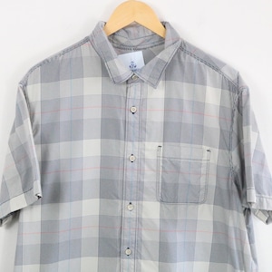 Puede incluir: Una camisa de manga corta con botones que presenta un patrón de cuadros en gris claro y gris oscuro con finas líneas de acento en rojo y azul. La camisa incluye un cuello estándar, una tapeta de botones frontal y un bolsillo en el pecho.