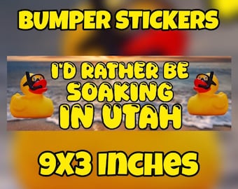 May include: A rectangular bumper sticker measuring 9x3 inches featuring a beach scene background with two yellow rubber ducks wearing black snorkels and masks. The text reads I'D RATHER BE SOAKING IN UTAH in bold yellow letters with a black outline.