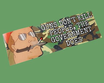 May include: A green, brown and black camouflage sticker with the text "Guns Don't Kill People, The Government Does". A cartoon character with a cigarette and a knife is in the background.