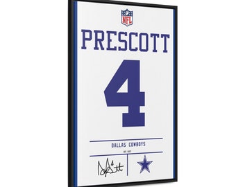 Può includere: Una stampa incorniciata della maglia del quarterback dei Dallas Cowboys, Dak Prescott. La stampa presenta uno sfondo bianco con il logo NFL, il nome di Prescott, il suo numero di maglia "4" e il nome della squadra Dallas Cowboys. La stampa include anche la firma di Prescott e il logo a stella dei Dallas Cowboys.